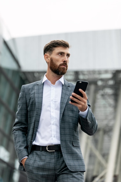 Biznesmen używa smartphone i ono uśmiecha się przy lotniskiem. Młody dyrektor wykonawczy z telefonem komórkowym przy lotniskiem.