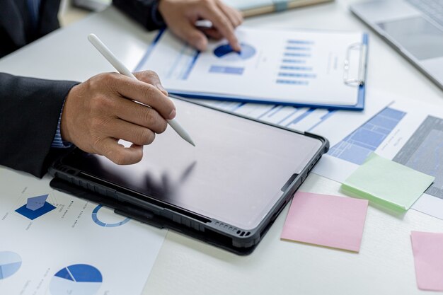 Biznesmen używa tabletu do porównywania informacji o dokumentach finansowych, sprawdza dokumenty finansowe firmy w biurze, sprawozdania finansowe firmy. Pojęcie zarządzania finansami.