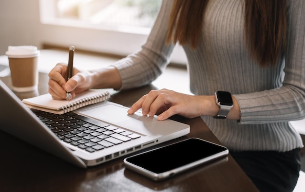 Biznesmen używający laptopa do pracy i pisania na notebooku z piórem w biurze z telefonem komórkowym obok laptopa