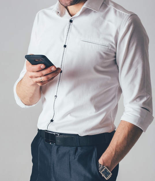 Biznesmen W Białej Koszuli I Czarnych Spodniach Trzyma Telefon W Ręku W Biurze. Mężczyzna Nosi Zegarek Na Rękę W Lewej Ręce