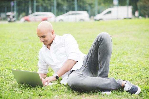 Biznesmen w białej koszuli pracy z laptopem na trawie w parku