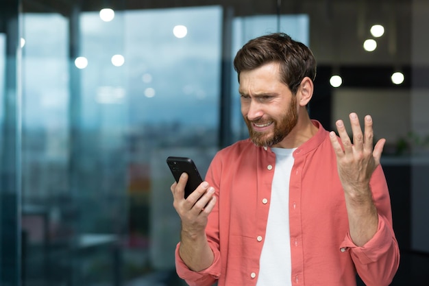 Biznesmen w czerwonej koszuli otrzymał złą wiadomość online na telefonie dojrzałego mężczyzny czytającego