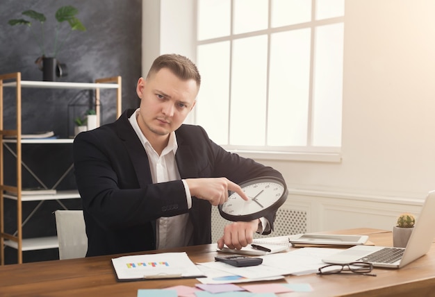 Biznesmen w garniturze trzyma zegar i wskazuje na to. Portret mężczyzny z zegarkami w biurze. Zarządzanie czasem i czasem to najcenniejsza koncepcja zasobów, kopia przestrzeń