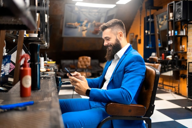 Biznesmen w garniturze za pomocą smartfona w salonie fryzjerskim