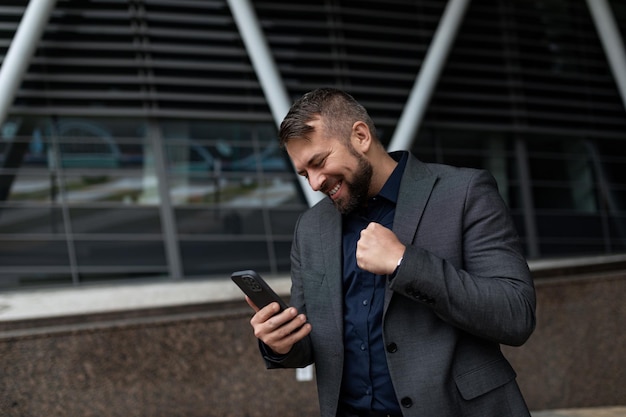 Biznesmen w klasycznym garniturze na tle biurowca z telefonem komórkowym w swoim