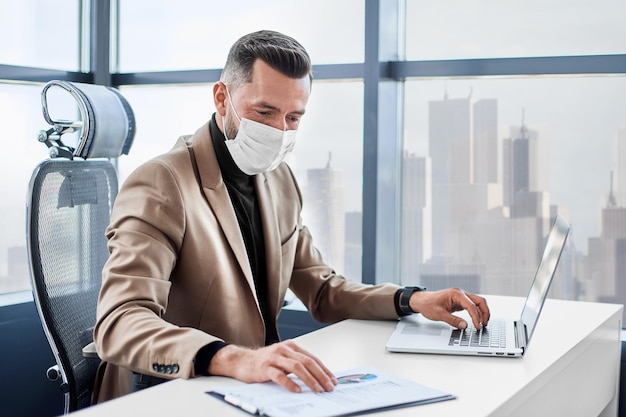 Biznesmen w masce ochronnej pracujący na laptopie w biurze