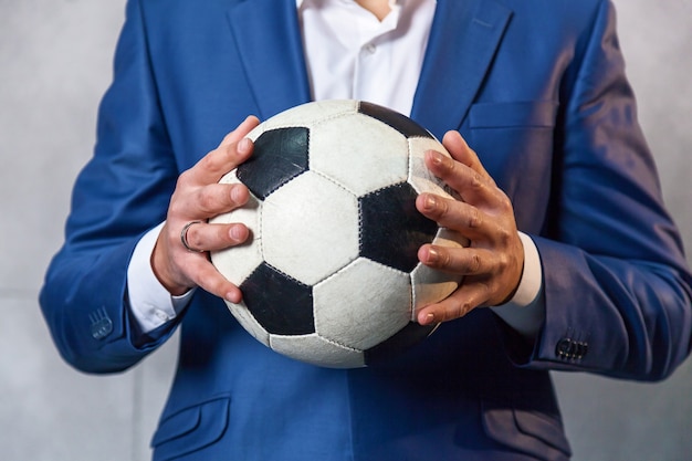 Biznesmen w niebieskim garniturze stoi pod ścianą i trzyma w ręku piłkę nożną.
