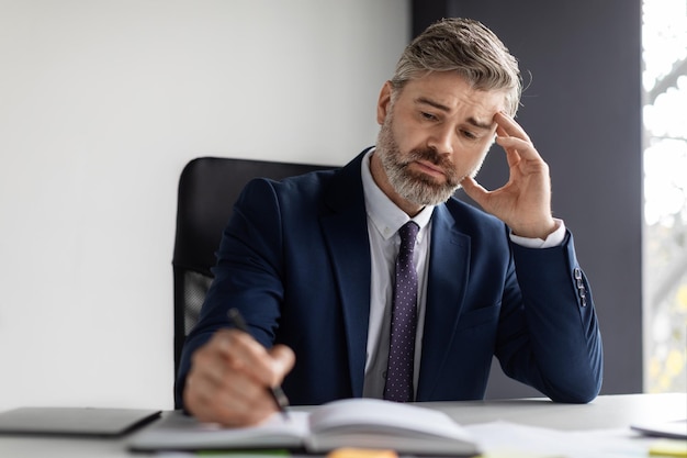 Biznesmen w średnim wieku siedzi przy biurku w biurze i pisze w notatniku