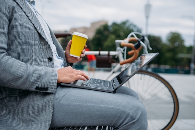 Biznesmen z cyklu pije kawę na ławce w biurowcu w centrum miasta.