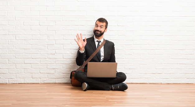 Biznesmen Z Jego Laptopa Siedząc Na Podłodze, Pozdrawiając Ręką Z Happy Wypowiedzi