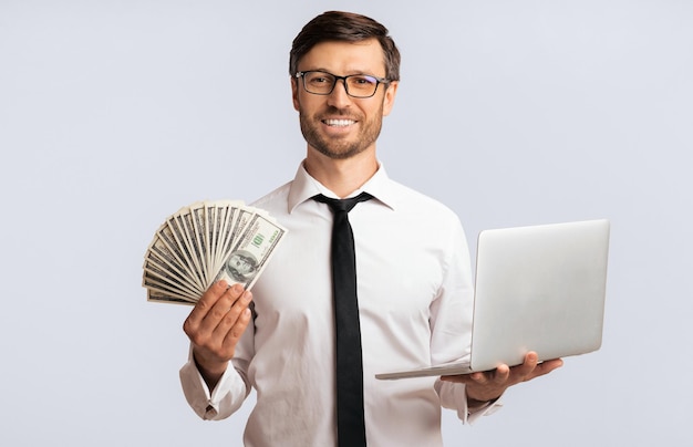 Biznesmen z laptopem i gotówką w studiu odizolowany