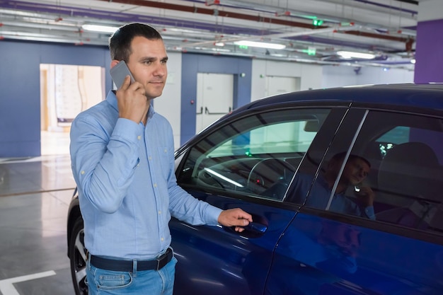 Biznesmen z telefonem w rękach blisko samochodu na podziemnym parkingu