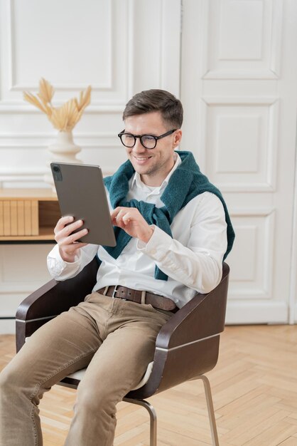 Biznesmen z zwykłym talentem wygodnie bada tablet siedzący w nowoczesnym