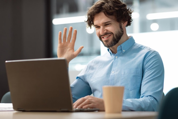 Biznesmen za pomocą laptopa macha ręką podczas rozmowy wideo