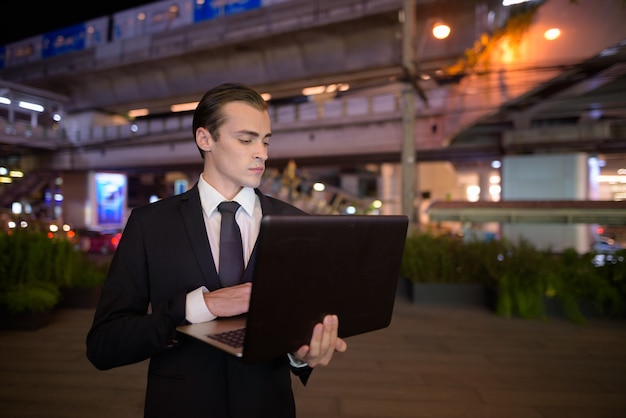 Biznesmen za pomocą laptopa na zewnątrz w nocy w mieście