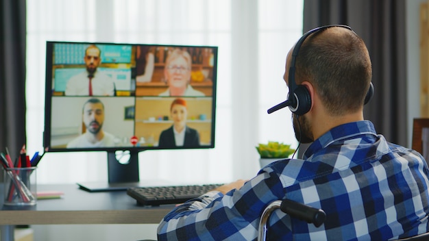 Biznesmen ze słuchawkami na wózku inwalidzkim podczas rozmowy wideo.