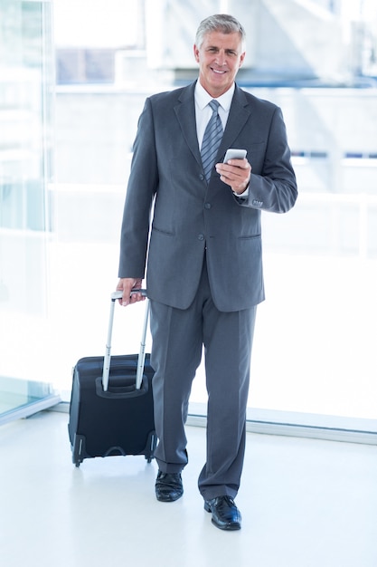 Biznesmena odprowadzenie z bagażem i używać jego smartphone