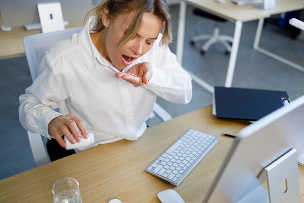 Biznesmenka w średnim wieku zażywająca tabletki w pracy