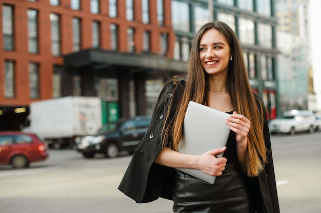 biznesowa dama w eleganckim stroju stoi na ulicy metropolii z laptopem w dłoniach