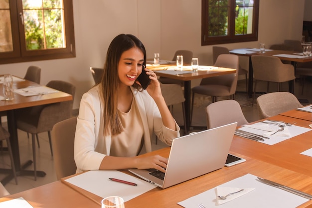 Biznesowa dziewczyna rozmawia przez telefon podczas pracy na laptopie w restauracji