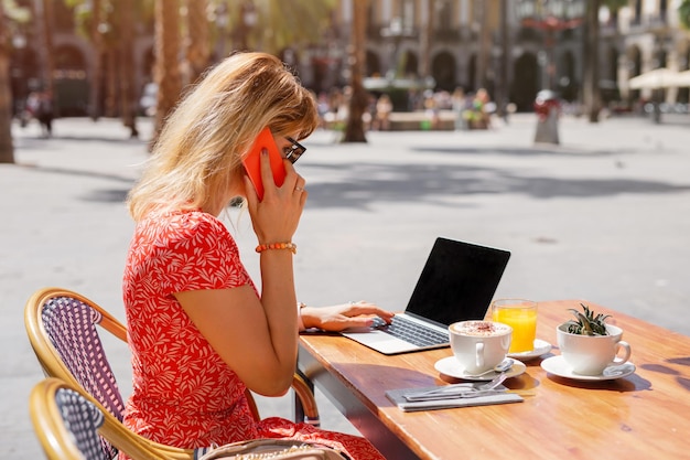 Biznesowa kobieta pracuje z laptopem i rozmawia przez telefon w kawiarni