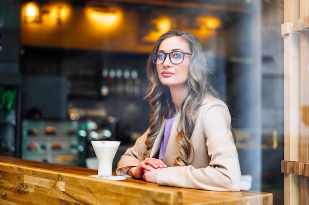 Biznesowa kobieta siedzi w kawiarni za oknem i czeka na partnera biznesowego