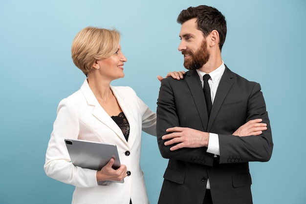 Biznesowa kobieta stojąca za swoim kolegą i dotykająca jego ramienia z przyjemnością uśmiechem na białym tle na niebieskim tle