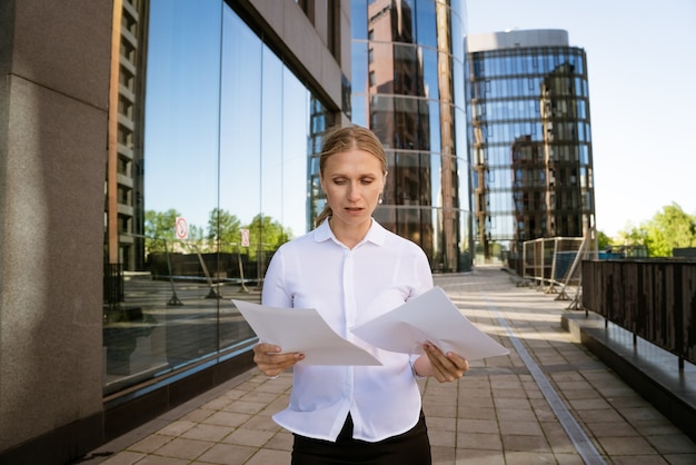 Biznesowa kobieta sukcesu z dokumentami w ręku na tle centrum biurowego