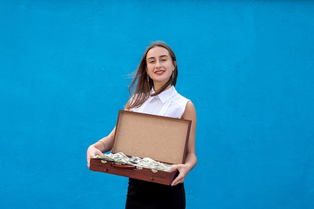 Biznesowa kobieta trzyma drewnianą walizkę pełny banknot dolarowy po sukcesie lub wielkim zwycięzcy na niebieskim tle