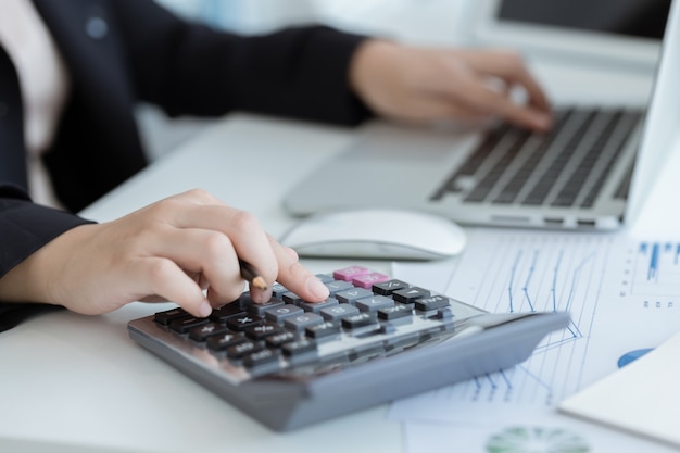 Biznesowa kobieta używa kalkulatora obliczać liczby na jego biurku w biurze.