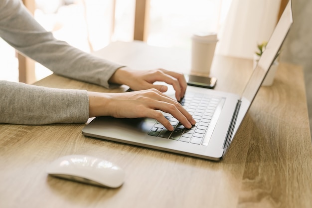 Biznesowa kobieta używa laptop robi online aktywności na drewno stołu biura w domu.