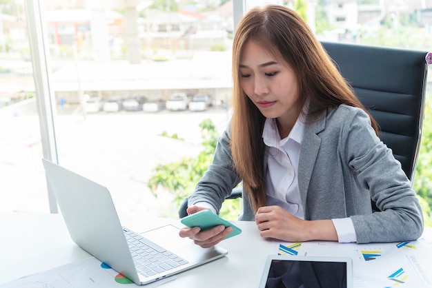 Biznesowa kobieta używa wiszącą ozdobę z laptopem na biurku w biurze.