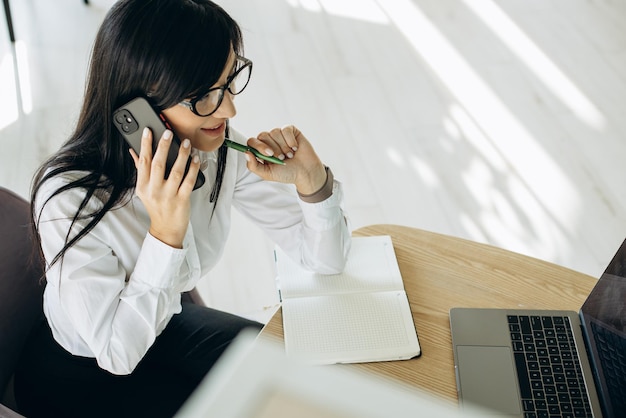 Biznesowa kobieta w biurze rozmawia przez telefon i pracuje na komputerze