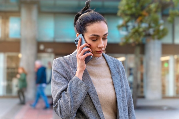 Biznesowa kobieta w kurtce i cajgach przecina drogę i rozmawia przez telefon