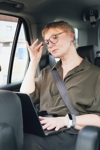 Biznesowa kobieta w okularach rozmawia przez telefon, siedząc na tylnym siedzeniu samochodu