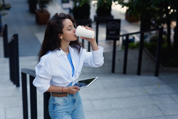 Biznesowa kobieta z kubkiem gorącej smacznej kawy stojąca na schodach w pobliżu centrum biznesowego