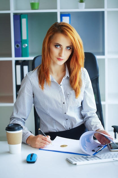 Biznesowa kobieta z rudymi włosami siedzi przy biurku w biurze Big Light