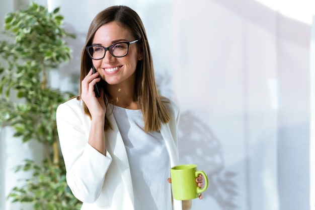 Biznesowa młoda kobieta używa jej telefon komórkowego w biurze.