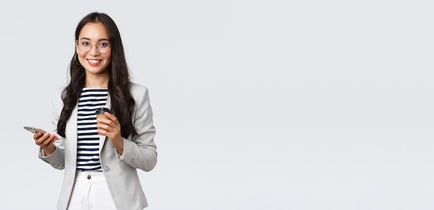 Biznesowe finanse i zatrudnienie koncepcja udanych przedsiębiorców Profesjonalna azjatycka bizneswoman w okularach spożywająca lunch pijąca kawę na wynos i używającą telefonu komórkowego