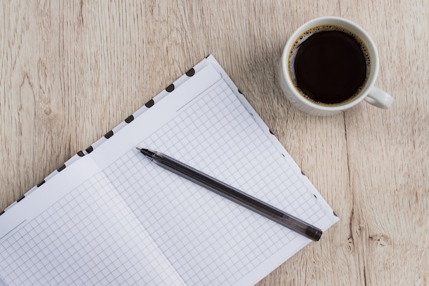 Biznesowy i biurowy pojęcie - otwiera pustego notatnika, pióro i filiżankę czarnej kawy na drewnianym stole. widok z góry.