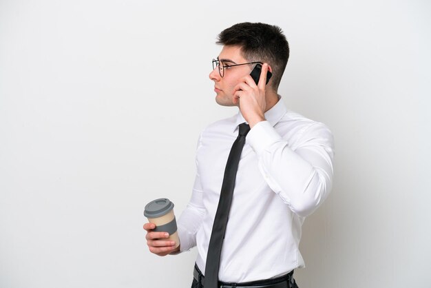 Biznesowy kaukaski mężczyzna na białym tle trzyma kawę na wynos i telefon komórkowy