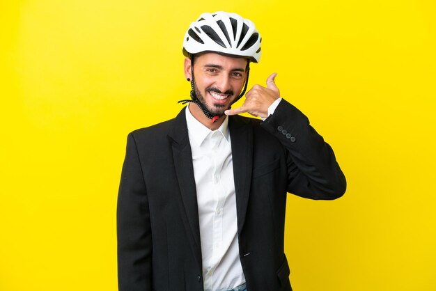 Biznesowy kaukaski mężczyzna z kaskiem rowerowym na białym tle na żółtym tle wykonujący gest telefoniczny Zadzwoń do mnie znak