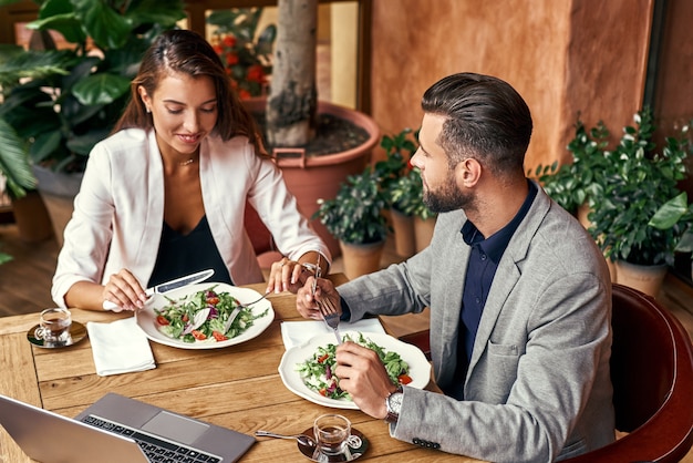 Biznesowy lunch mężczyzna i kobieta siedzą przy stole w restauracji jedzą zdrową świeżą sałatkę rozmawiają