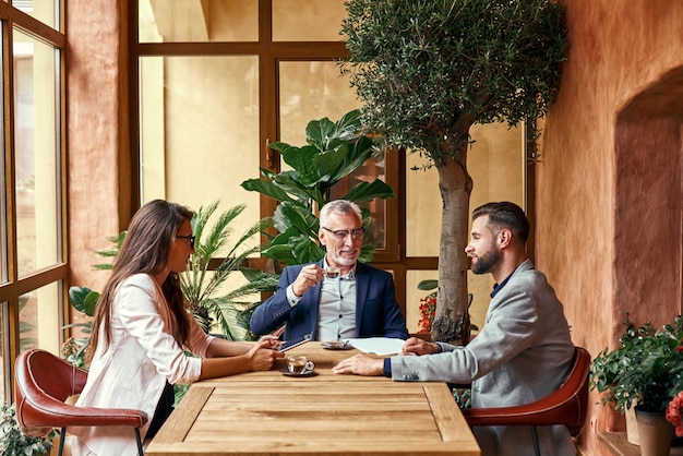 Biznesowy lunch trzy osoby w restauracji siedzące przy stole, pijące gorącą kawę, dyskutujące