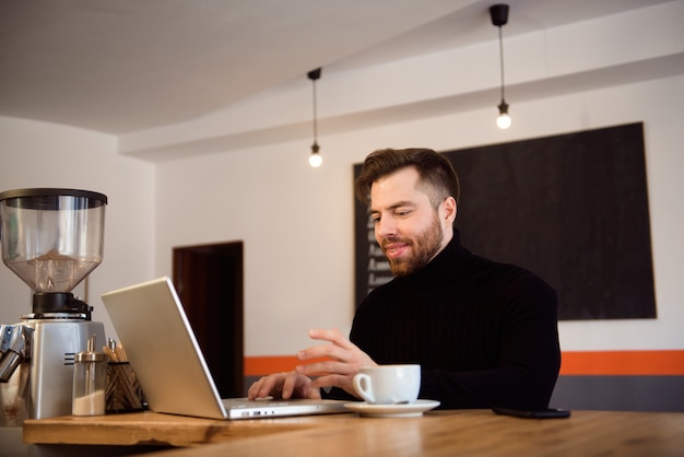 Biznesowy mężczyzna ma kawę w sklep z kawą i pracuje na jego laptopie.