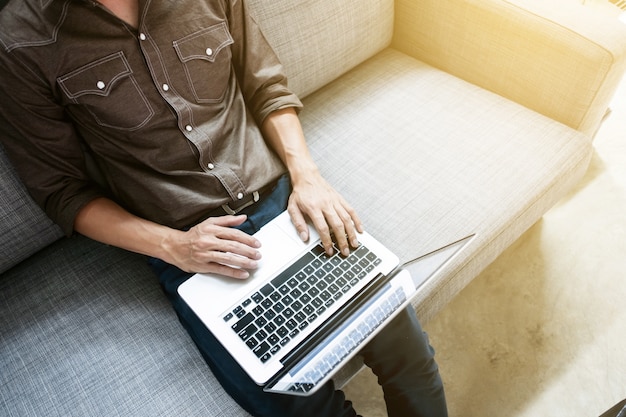 Biznesowy mężczyzna wewnątrz relaksuje przypadkową formę pracuje z laptopu obsiadaniem na kanapie przy biurem