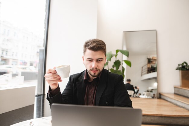 Biznesowy mężczyzna z filiżanką kawy w jego rękach siedzi w restauraci i pracuje na laptopie. Pracuj na lunchu w restauracji