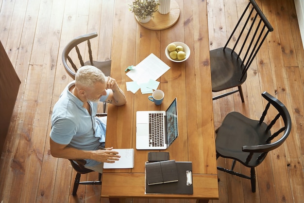 Biznesowy widok z góry online dojrzałego kaukaskiego mężczyzny pracującego na laptopie, siedzącego przy stole w jego