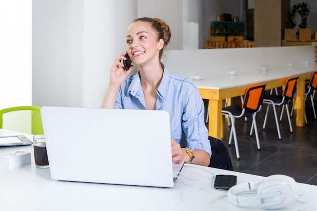 Biznesu, Technologii I Zieleni Biurowy Pojęcie, - Młody Pomyślny Bizneswoman Opowiada Na Telefonie Przy Biurem Z Laptopem. Piękna Kobieta Używa Pastylka Komputer.