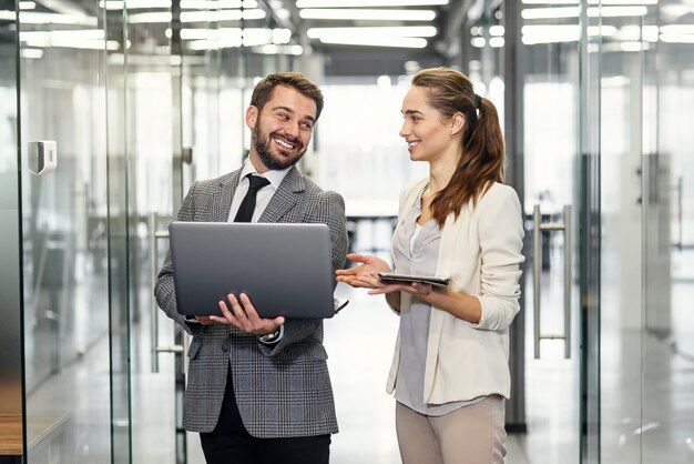 Bizneswoman I Biznesmen W Laptopie Stoi Projekt W Pustych Biurowych Okno Z Miasto Widokiem I Dyskutuje.